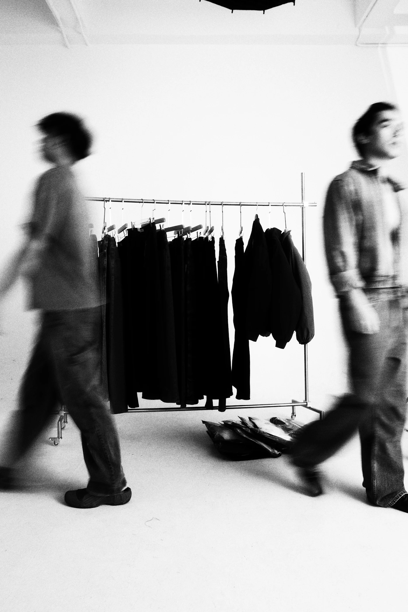 Duas pessoas passam por uma arara de roupas, em preto e branco